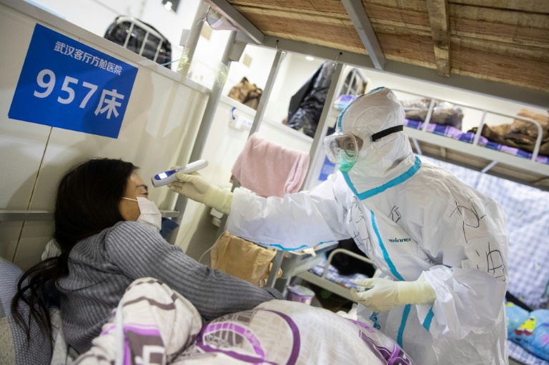 Um membro da equipe médica (e) que verifica a temperatura corporal de um paciente que apresentou sintomas leves do coronavírus, em um centro de exposições convertido em um hospital em Wuhan