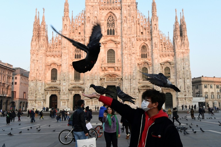 Homem usando uma máscara protetora brinca com pombos na Piazza del Duomo, no centro de Milão, após medidas de segurança tomadas no norte da Itália contra o COVID-19, o novo coronavírus