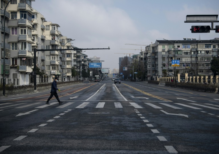Homem com uma máscara protetora atravessa uma rua vazia na cidade chinesa de Hangzhou, cerca de 175 km a sudoeste de Xangai