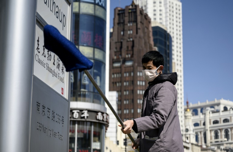 Homem com uma máscara protetora limpa um painel com logotipos de companhias em frente a um edifício de Xangai, em 18 de fevereiro de 2020