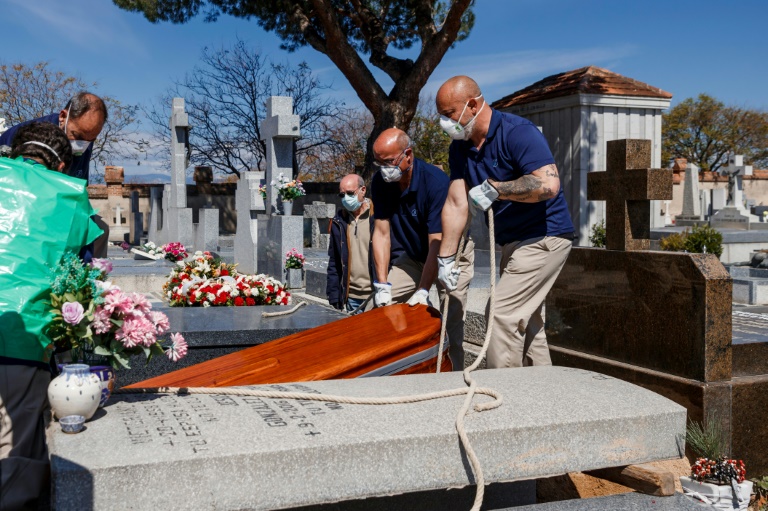 Funcionários de funerária, com máscaras, enterram caixão de vítima da COVID-19 no cemitério de Fuencarral, em Madri, em 29 de março de 2020