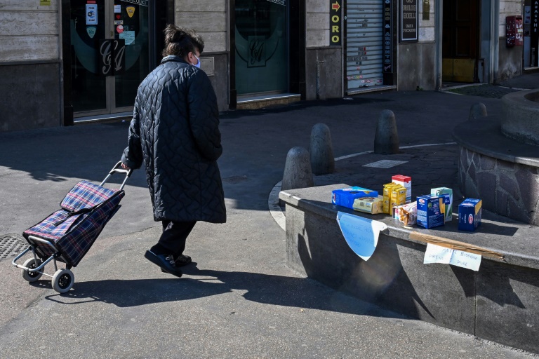 Mulher passa por pacotes de alimentos colocados por moradores em um banco público na Piazza dell'Aberone em Roma, como parte de uma iniciativa para ajudar os pobres durante quarentena