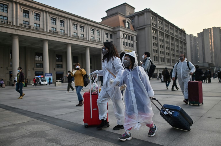 Passageiros com máscaras faciais e trajes completos para se proteger de coronavírus chegam na Estação de Wuhan, no centro da China