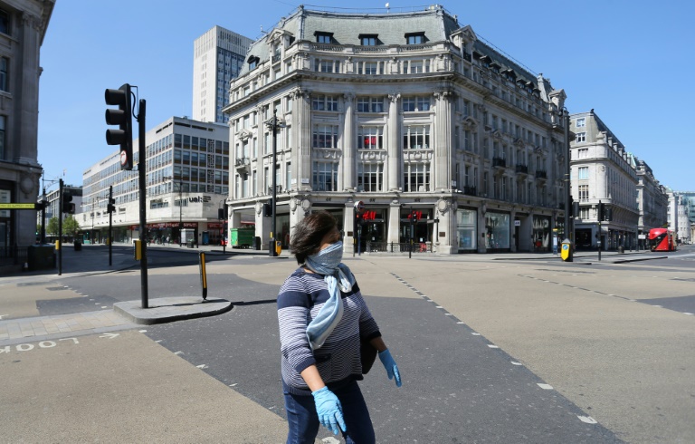 Mulher usando equipamento de proteção individual, incluindo luvas e um lenço como máscara facial, atravessa rua vazia em Londres, em 21 de abril de 2020