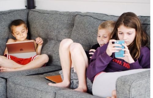 Dois pais felizes ensinando o filho a usar o aplicativo online no celular.  menino jogando o jogo no celular. família em casa e conceito de comunicação