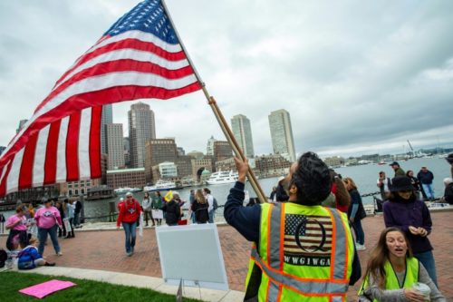 Um homem com um colete QAnon agita uma bandeira dos EUA enquanto manifestantes se reúnem em 5 de outubro de 2020 para protestar contra as vacinas obrigatórias contra gripe para crianças em Boston, Massachusetts