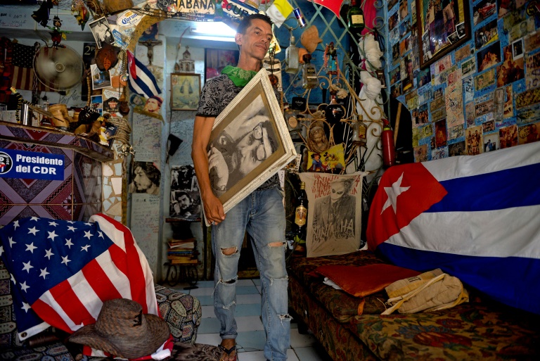 Nesta foto de 07 de agosto de 2020, um homem carrega um retrato do líder cubano Fidel Castro ao lado das bandeiras cubana e norte-americana em sua casa em Havana, em 29 de julho de 2020