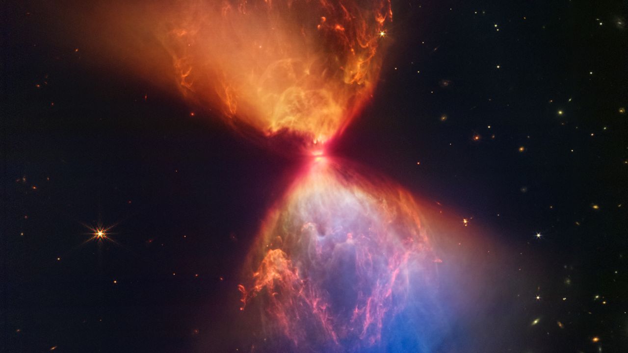 A protoestrela em torno da qual a imagem gira está escondida no pescoço de uma nuvem escura de gás e poeira em forma de ampulheta.