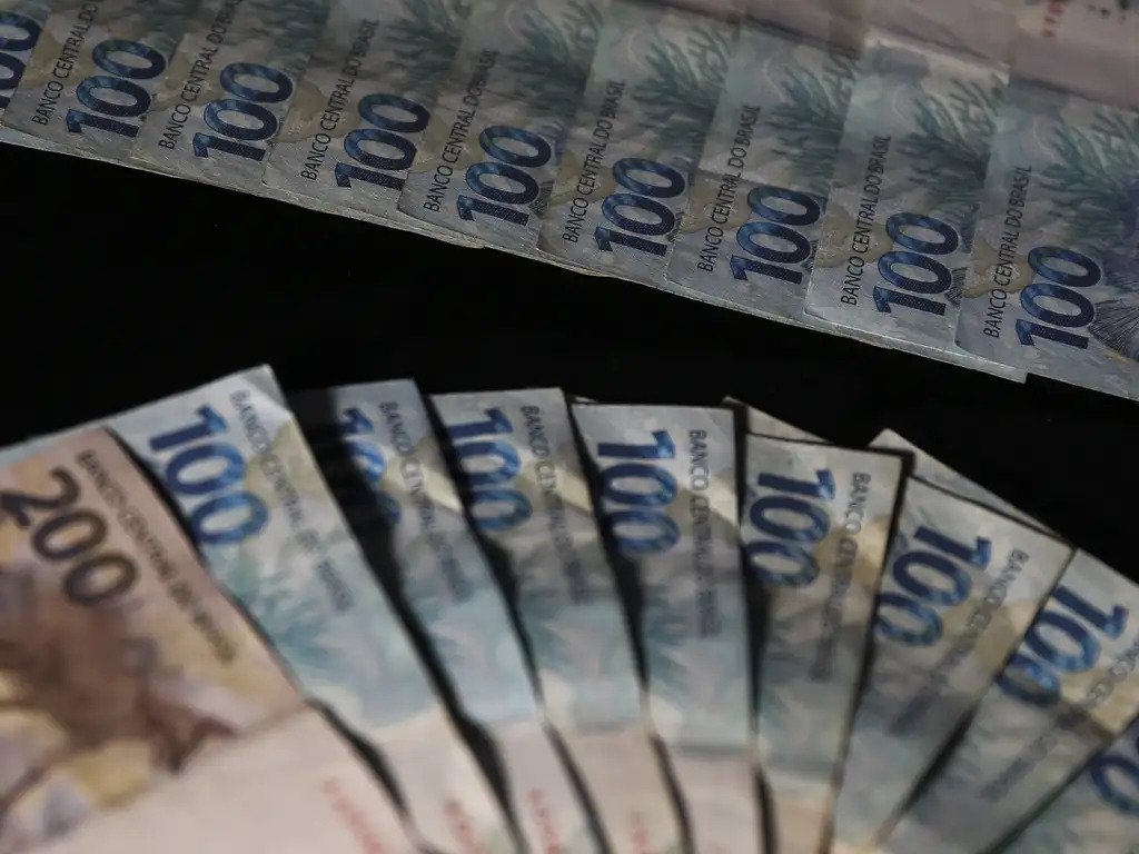 Notas de R$ 100 e R$ 10 empilhadas, simulando uma contagem de R$ 100 mil