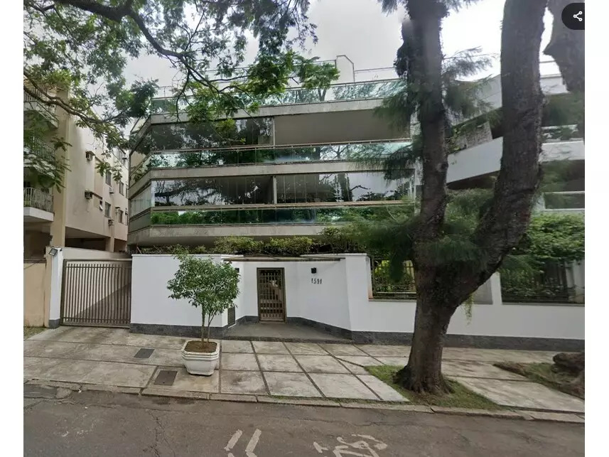 Foto da fachada de um apartamento disponível em um dos leilões. É um apartamento de sacada ampla, em um prédio branco, com uma árvore em frente