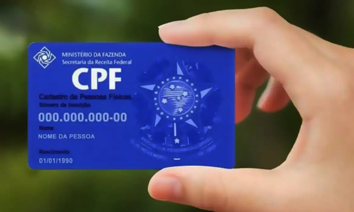 Consultar CPF. Fotografia mostra um cartão de CPF segurado entre dois dedos de uma pessoa