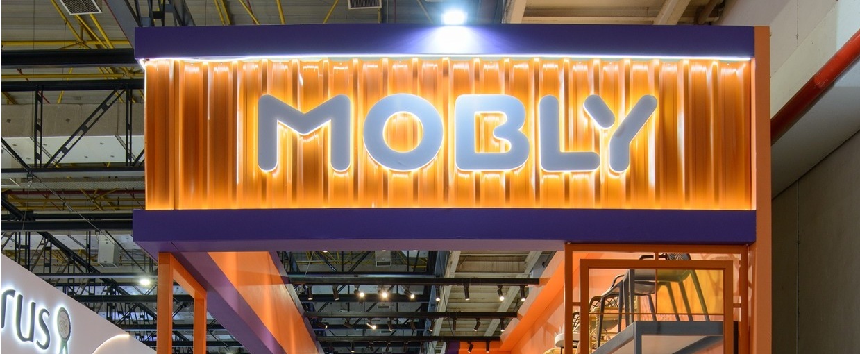 Logo da Mobly aparece em um estande de móveis decorados