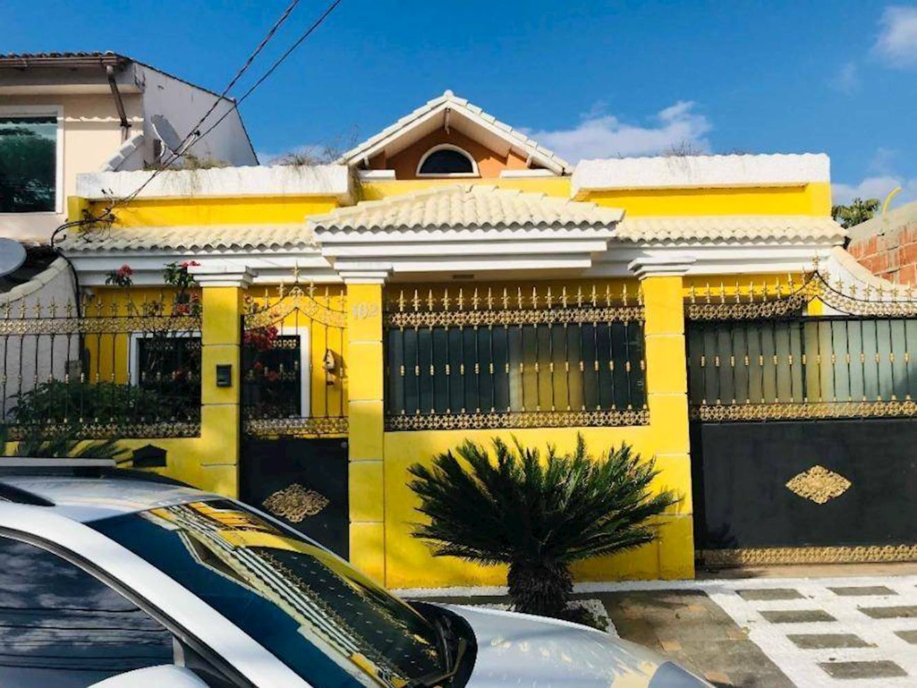 Fotografia do imóvel de um dos leilões. É uma casa amarela, com um coqueiro baixo em frente