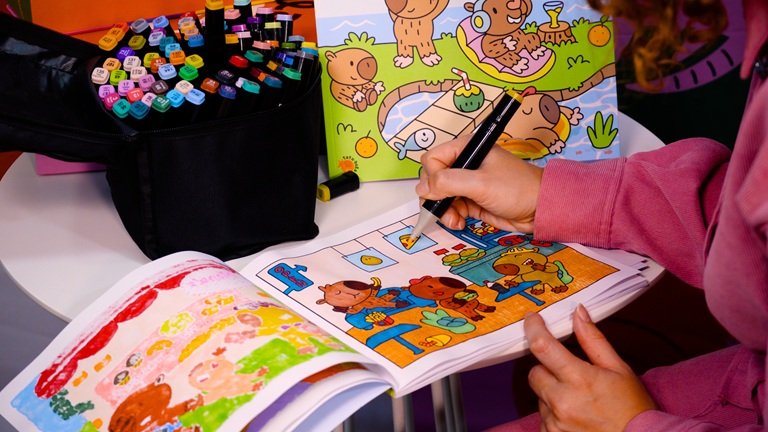 Fotografia de uma pessoa a pintar um livro CapyVibes com canetinhas, assim como fazem com a franquia Bobbie Goods