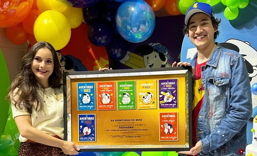 Manu Digilio e Gabriel Dearo seguram placa comemorativa de 1 milhão de cópias vendidas da franquia "As aventuras de Mike"