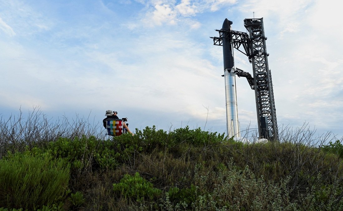 Um fotógrafo observa enquanto a espaçonave Starship da SpaceX é içada pela torre de lançamento para ser empilhada sobre o propulsor pesado, em preparação para seu 10º voo de teste, a partir do complexo da empresa em Starbase, Texas, EUA, em 23/08/2025