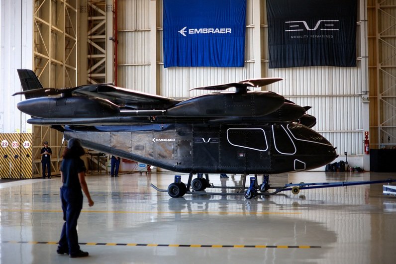 Funcionários ficam perto do protótipo em escala real da aeronave elétrica de decolagem e pouso vertical (eVTOL) desenvolvida pela Eve Air Mobility, uma empresa do grupo Embraer, enquanto ela é apresentada pela primeira vez em Gavião Peixoto, Brasil, em 3 de julho de 2024.