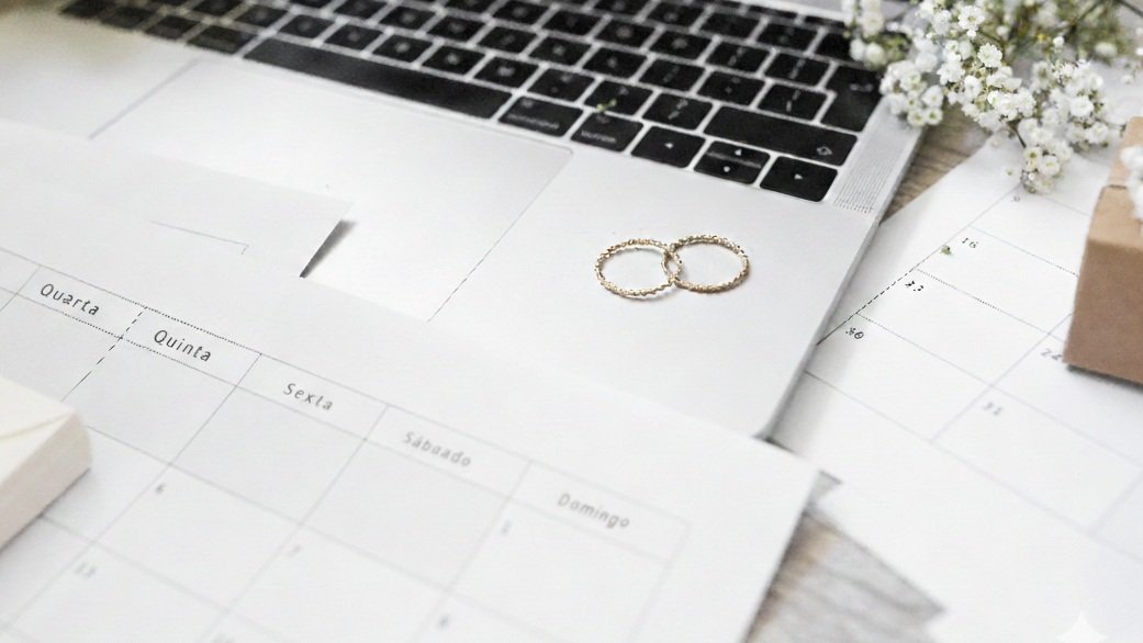 Fotografia de um par de alianças sobre um computador e um calendário para matérias sobre casamento