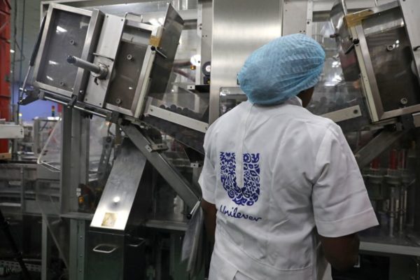 Uma mulher está atrás de uma máquina que faz parte de uma linha de fabricação de pasta de dente na fábrica da Unilever em Lagos, Nigéria