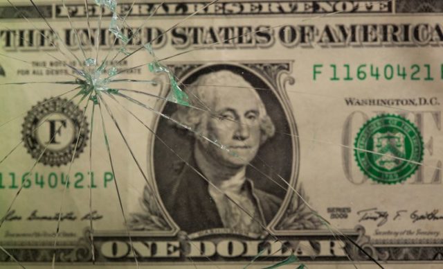 Nota de dólar vista através de uma vidraça quebrada