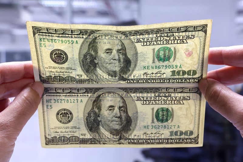 Funcionário de banco compara nota falsa de dólar (embaixo) com nota verdadeira (em cima) em agência bancária em Bangkok, Tailândia