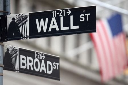 Placa de Wall Street em frente a bandeira dos EUA, do lado de fora da Bolsa de Valores de Nova York; investir