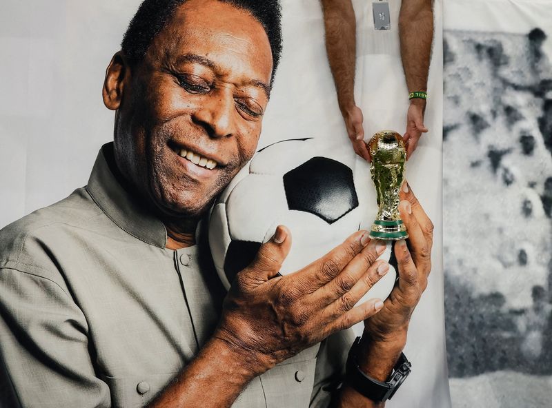Torcedor brasileiro segura réplica do troféu da Copa do Mundo ao lado de faixa com a foto da lenda do futebol Pelé no Estádio Lusail, antes de partida entre Brasil e Camarões pela Copa do Mundo do Catar