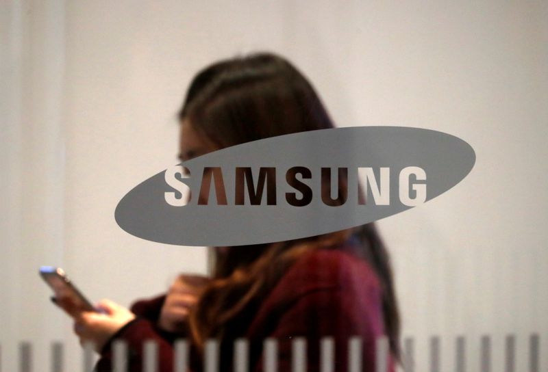 Mulher confere seu smartphone atrás de logotipo da Samsung. 7/1/2019
