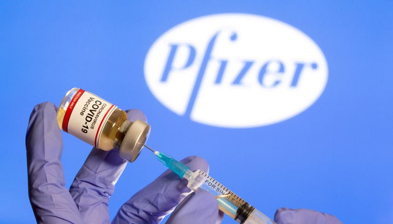 Mulher segura frasco rotulado como de vacina contra Covid-19 em frente ao logo da Pfizer em foto de ilustração