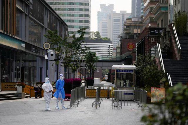 Funcionários em trajes de proteção caminham em rua de Xangai durante lockdown para conter disseminação da Covid-19